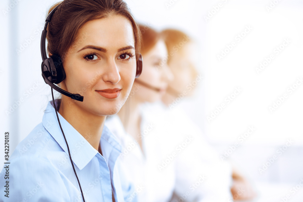 Call center operators. Focus on beautiful business woman using headset in sunny office Call center operators. Focus on beautiful business woman using headset in sunny office