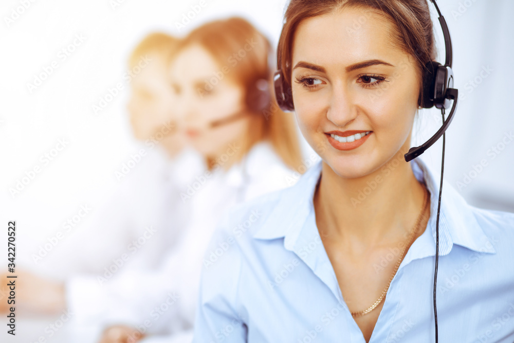 Call center operators. Focus on beautiful business woman using headset in sunny office Call center operators. Focus on beautiful business woman using headset in sunny office