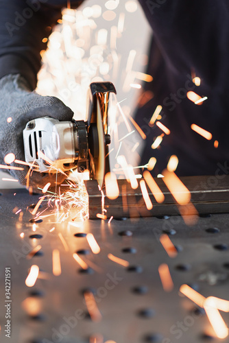 A metal worker cuts a rectangular metal pipe with an angle grinder