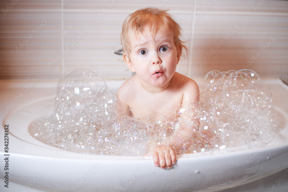 Funny child playing with water and foam in a bathroom.