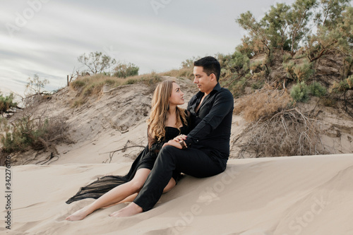 Sexy couple sitting on the beach sand talking, looking each other straight in the eyes. Black formal shirt and pants