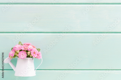 Small pink flowers in decorative vase in shape of watering can on wooden background. Flat lay, top view, copy space.