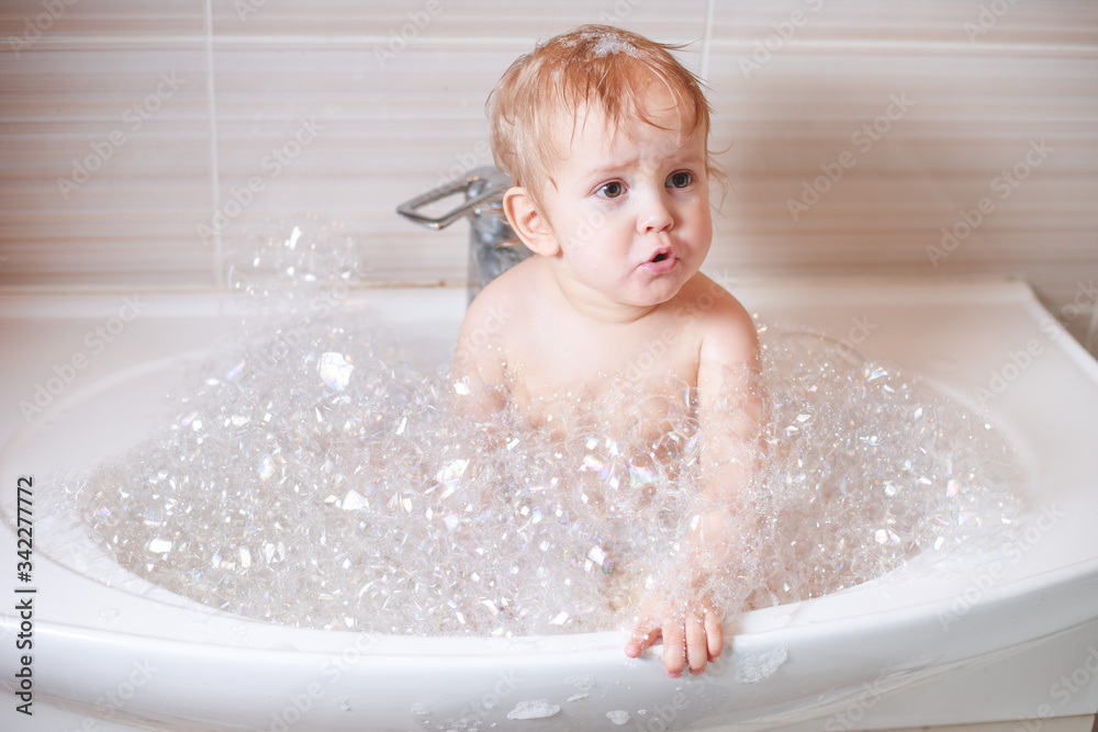 Happy laughing Infant baby toddler taking a bath playing with foam bubbles. Children care and hygiene concept. Happy laughing Infant baby toddler taking a bath playing with foam bubbles. Children care and hygiene concept.