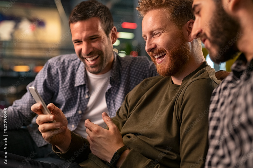 Friends laughing and using smartphone at pub Friends laughing and using smartphone at pub