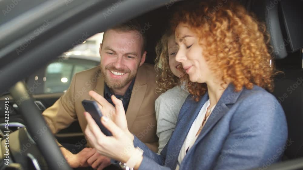 Happy caucasian family now the owners of new representative car. Family made purchase in dealership, enjoy having new automobile.