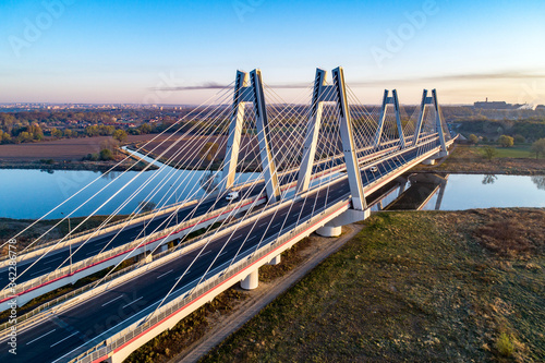 New modern double cable-stayed bridge with wide three-lane roads over Vistula River in Krakow, Poland, and its reflection in water at sunrise. Part of the ring road around Krakow. Aerial view