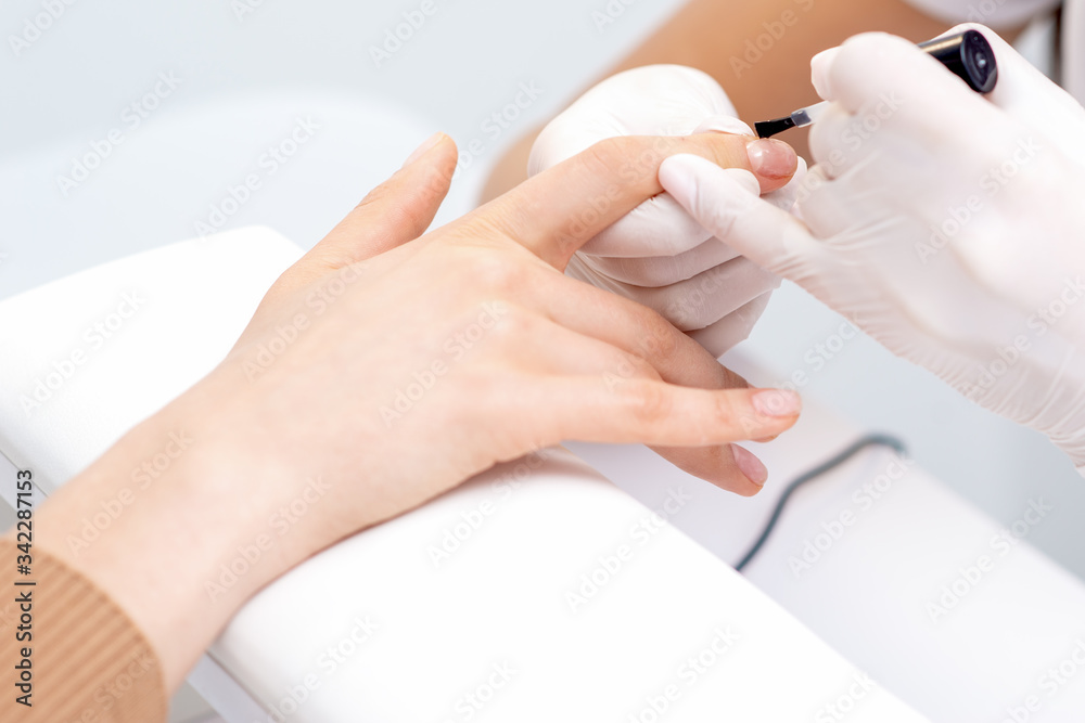 Hands of manicurist are covering clear varnish to nail of woman in manicure salon. Hands of manicurist are covering clear varnish to nail of woman in manicure salon.