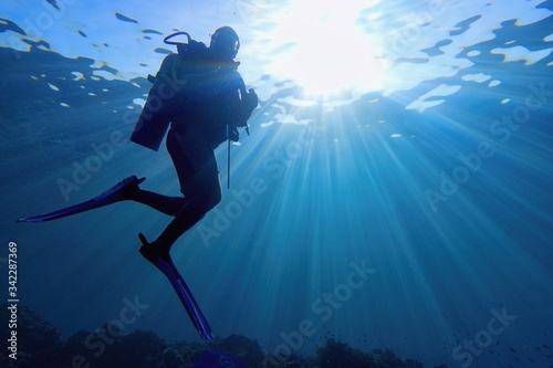 Life-giving sunlight underwater. Sun beams shinning underwater and Scuba diver silhouette in the blue water