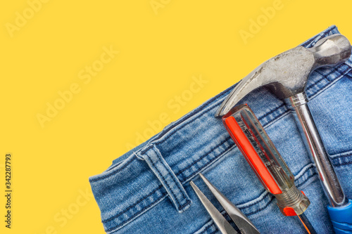 Jeans, screwdriver, hammer and pliers on yellow background. Jeans texture, Blue denim jeans with tools. Copy space concept