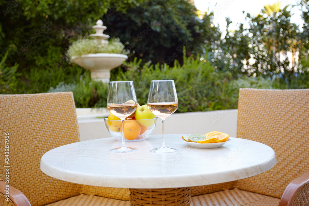 Two glasses of white wine and fresh fruit stand on a table on the terrace of an outdoor cafe. Romantic dinner for two in the open air