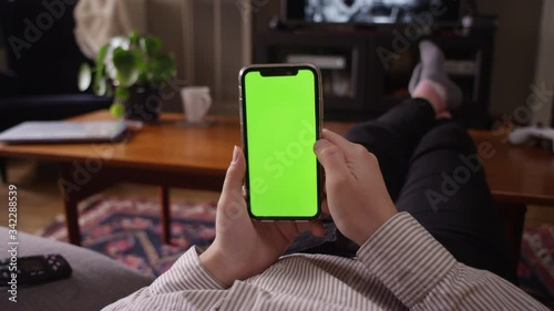 POV of a woman scrolling through her smartphone with the television on in the background