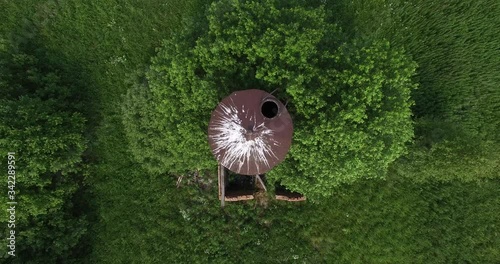 4K aerial summer morning high quality video footage of old unused rusty metal water pressure tower among lush green vegetation in European landscape