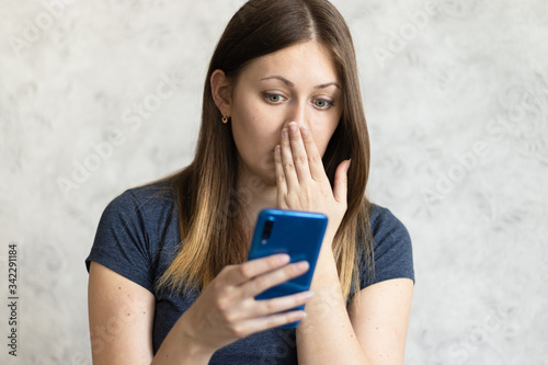 Woman watching shocking video online on her mobile phone. Young girl looking at phone seeing bad news or photos. Girl pleasantly surprised and excited photo