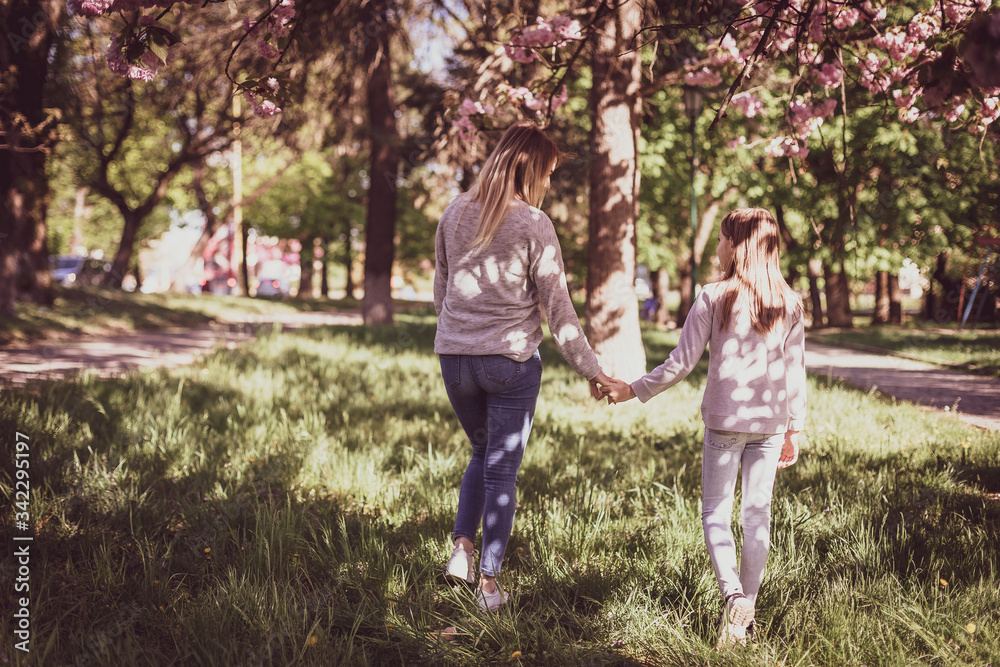 Sakura blossomed. Young mother with her child have fun in the park near the sakura. Spring morning. They look at each other Sakura blossomed. Young mother with her child have fun in the park near the sakura. Spring morning. They look at each other