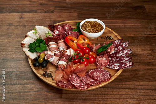 many types of sausages with vegetables and olives on a wooden plate