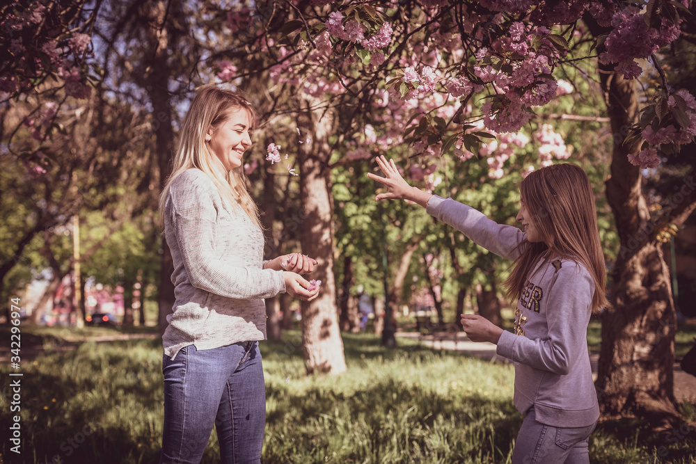 Fototapeta premium Sakura blossomed. Young mother with her child have fun in the park near the sakura. Spring morning. They look at each other