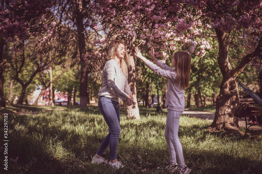 Fototapeta premium Sakura blossomed. Young mother with her child have fun in the park near the sakura. Spring morning. They look at each other