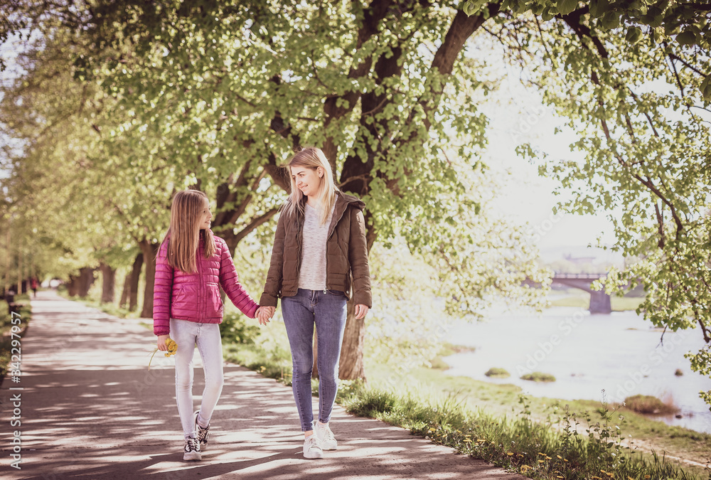 Young mother with baby walking in park near river. Spring morning. They look at each other Young mother with baby walking in park near river. Spring morning. They look at each other