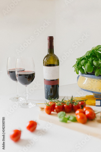A bottle of red wine, two glasses, cherry, spaghetti and basil in the frame. Italian food concept.