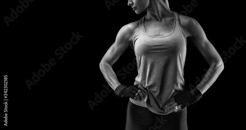 Fitness woman in sports tank top, short sleeve tee, gloves. Black and white close-up photo with copy space on left. Her hands on hips.