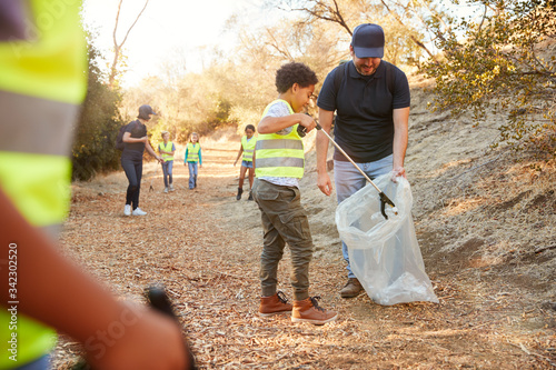 Adult Team Leader With Group Of Children At Outdoor Activity Camp Collecting Litter Together