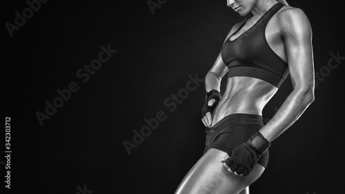 Fitness sporty woman showing her well trained body. Strong abs showing. Sensual young female posing in black background with copy space. Black and white close-up photo.