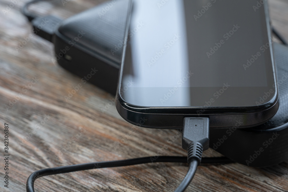 Smartphone charging with power bank on wood board. Phone Connected to charger Smartphone charging with power bank on wood board. Phone Connected to charger