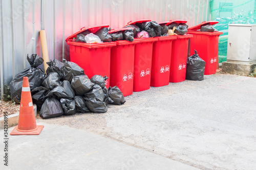 group red bins six with symbol infectious and garbage bag black pile On top in the outdoors. concept prevent infection coronavirus (covid-19)