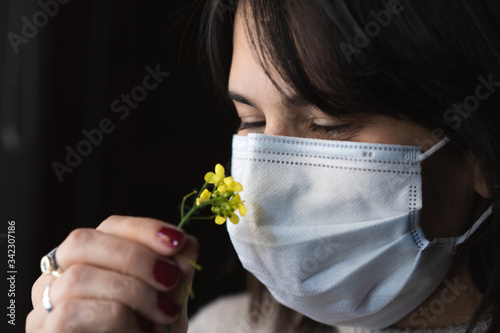 mujer oliendo una flor con un barbijo en cuarentena woman smelling a flower with a chin mask photo