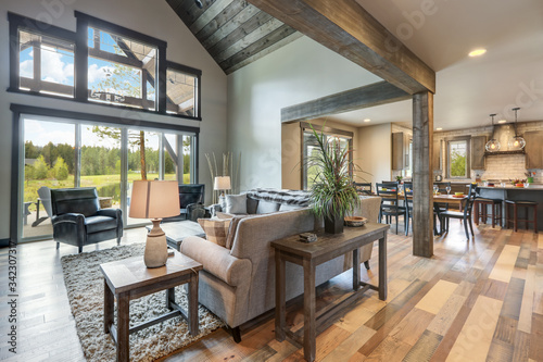 Living room luxury interior with large stone fireplace and leather furniture and huge tall windows with natural tones with TV.