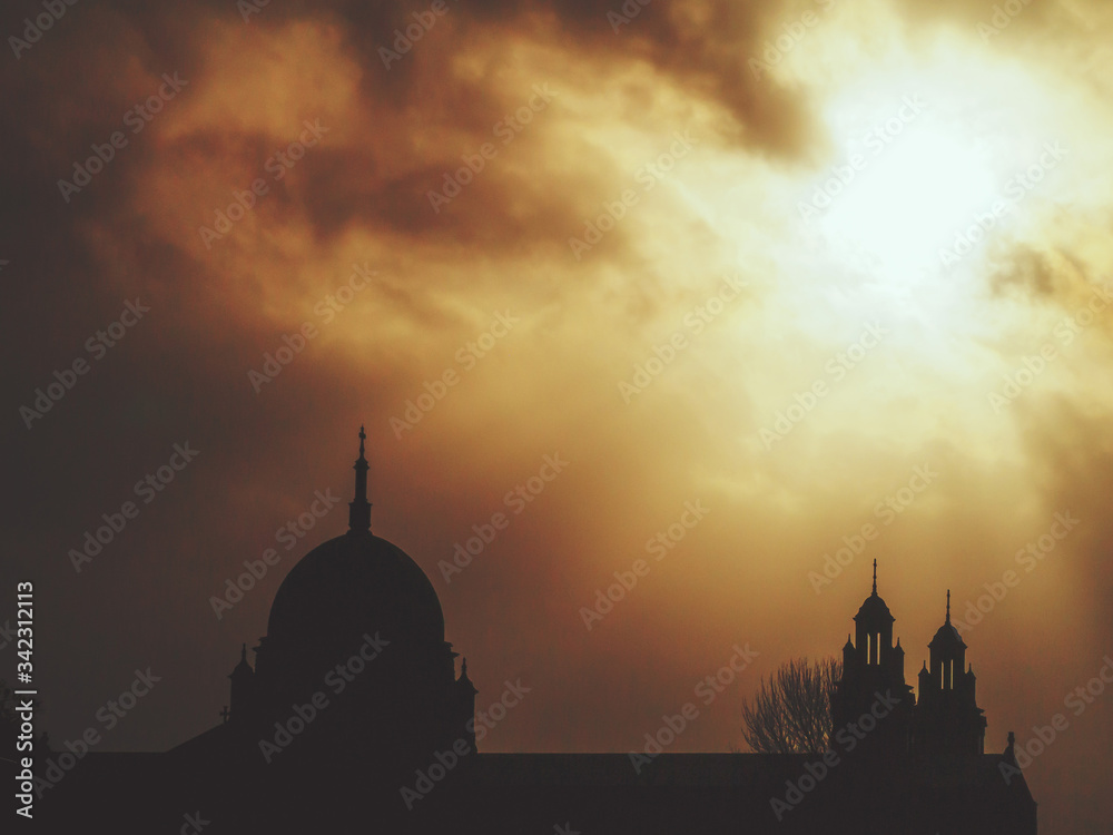 Silhouette of dome of Galway Cathedral , dramatic cloudy sky in the background with light rays bursting through the clouds. Warm orange tone.