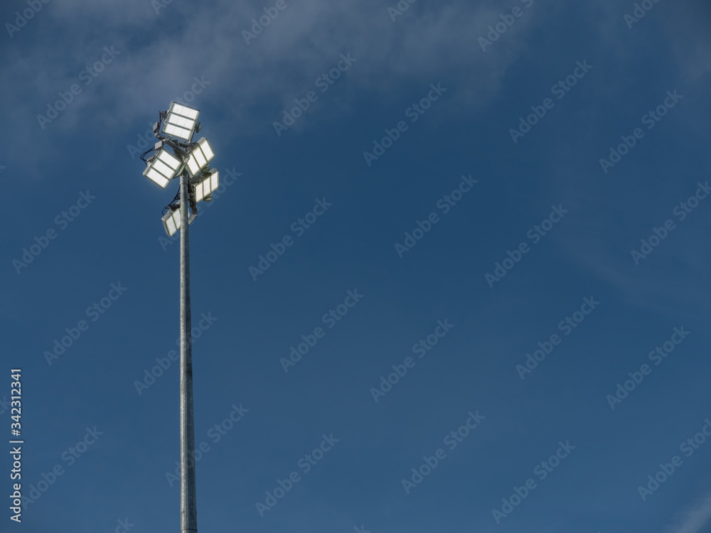 Powerful LED light on a metal pole turned on, cloudy sky background. Concept sport event, game.