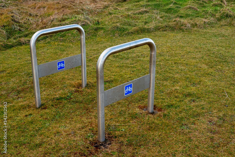 Two metal chrome bicycle stands on a grass in a town park. Two metal chrome bicycle stands on a grass in a town park.
