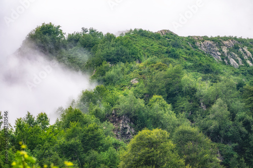 High mountain with green rocky slopes hidden in clouds and fog.