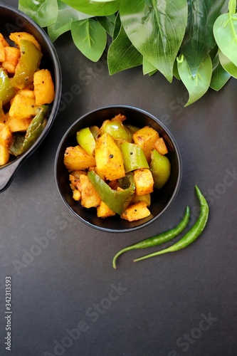 Indian food - Spicy Capsicum and potato stir fried with Indian spices. Aloo and Shimla Mirchi. served in the black plate over white background. 