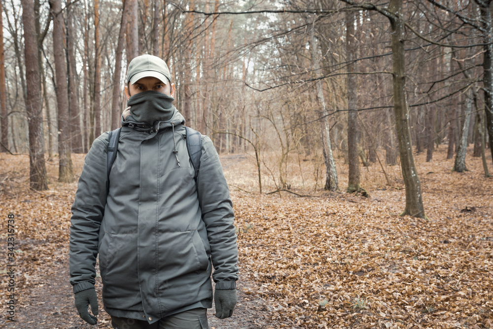A man with a covered face walking through the autumn forest
