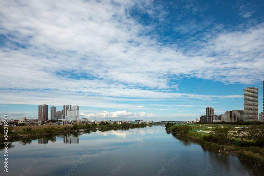 多摩川の川面を挟んで向かい合う川崎武蔵小杉ビル群と東京大田区側。多摩川に架かるガス橋から上流側を見た風景。