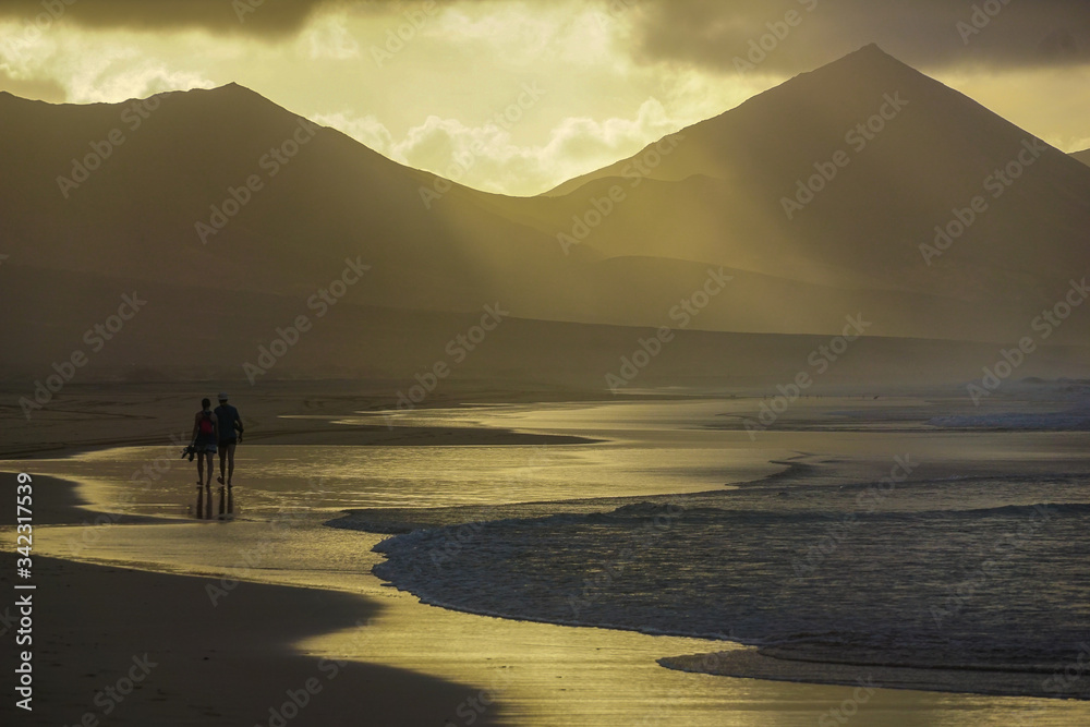 COFETE BEACH,FUERTEVENTURA - JANUARY 19, 2020: A couple is walking in the sand towards the sunset on the edge of the waves