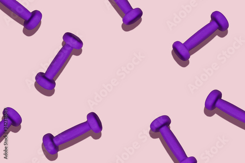 Sports pattern. Purple dumbbells scattered on a pink mat. The circle in the center of the frame for the text.