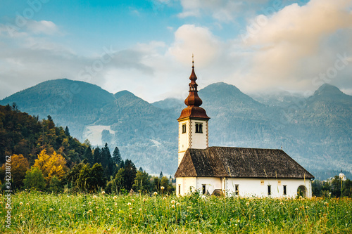 White church standing in a green meadow under high mountains. White church in slovenian alps.