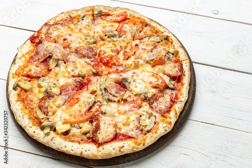 Pizza Francesca with cheese, champignon mushrooms, tomatoes and sliced meat on a white wooden background.