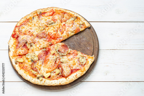 Pizza Francesca with cheese, champignon mushrooms, tomatoes and sliced meat on a white wooden background.