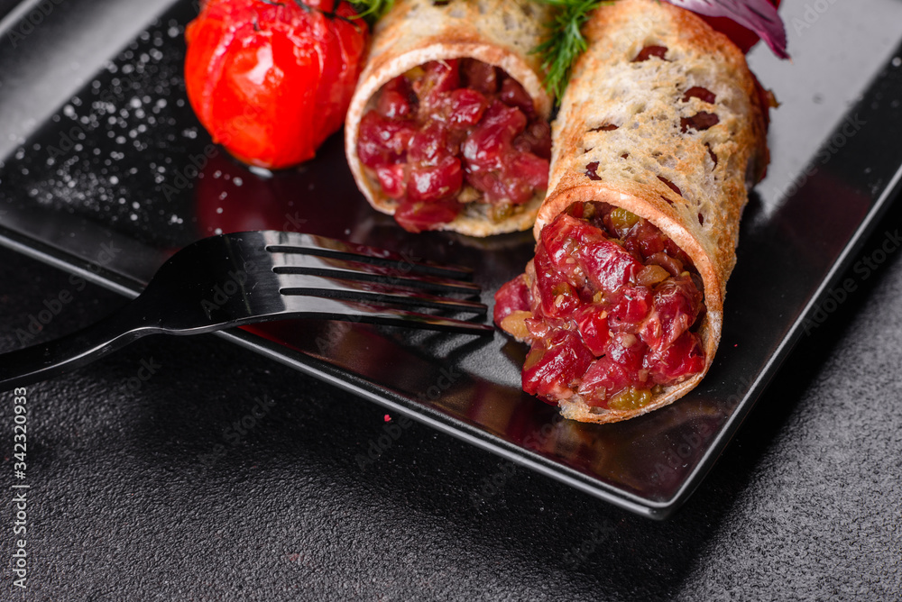 Delicious fresh beef tartar with toasts on a black square plate Delicious fresh beef tartar with toasts on a black square plate