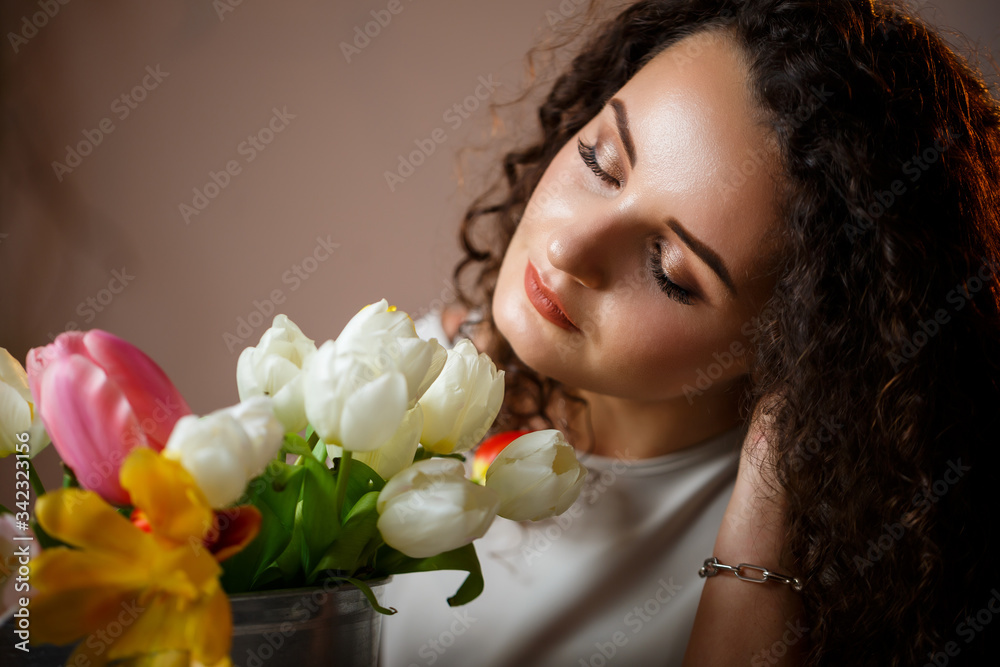 Portrait of a curly girl with a bucket of tulips. Fresh flowers for beautiful photos. Delicate photos with flowers in the studio