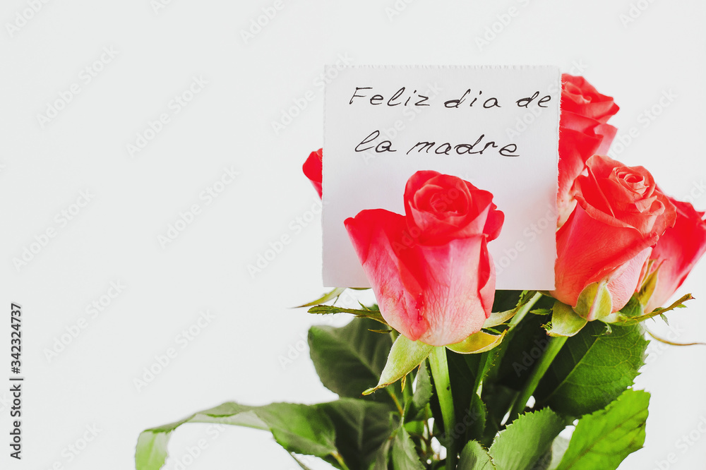 Fototapeta premium Mother's day greeting card on white background: Bouquet of small roses and a handwritten gift card with the inscription Happy Mother's Day in Spanish 