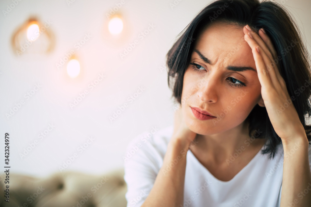 Tension headache. Close-up photo of a woman in distress, who is touching her forehead and her neck while looking aside.