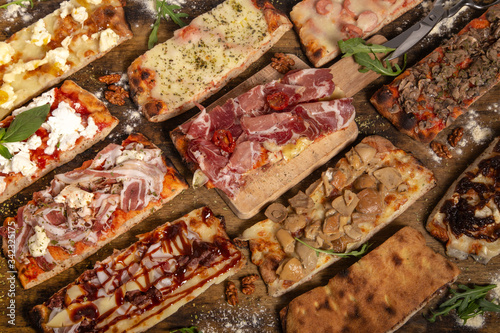 Assortment of rectangular homemade rustic pizza slices on wooden table.