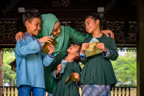 Happy children holding an envelope of pocket money or raya angpao from their mother during Eid al-Fitr celebration. Malaysian Family and Raya Concept.