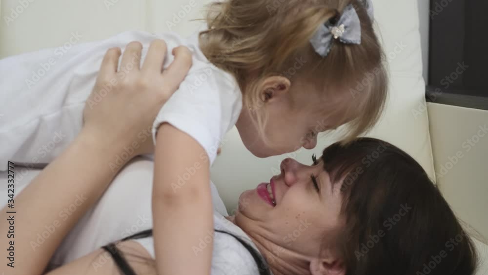 Happy family. A young mother with a blonde daughter play on the couch at home, a girl holds a laughing child in her arms. Happy family. A young mother with a blonde daughter play on the couch at home, a girl holds a laughing child in her arms.