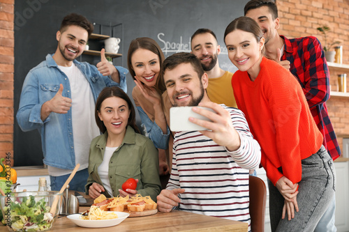 Young friends taking selfie while cooking together at home